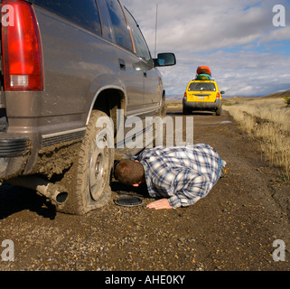 Man lays on the muddy road to change a flat tire on his SUV Stock Photo