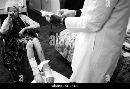 A district nurse puts on surgical gloves before changing the dressing of an elderly patient during a visit to a care home. Stock Photo
