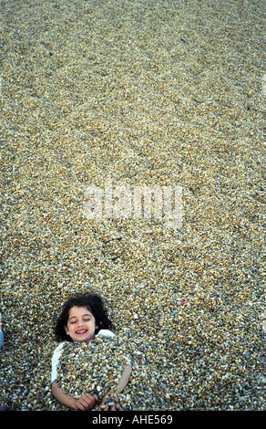 Girl buried in pebbles on beach Stock Photo: 24210308 - Alamy