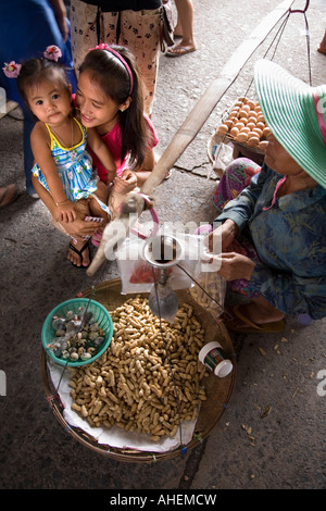 Street vendor selling peanuts and eggs with customer and small Thai child in Banchang market, Thailand. Stock Photo