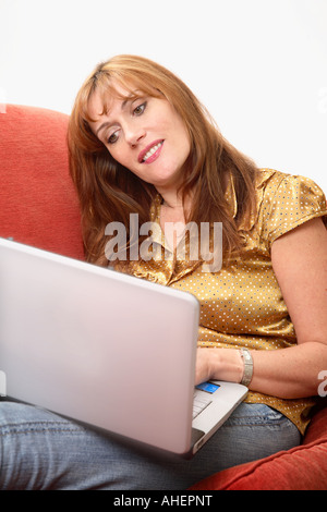 Woman using a laptop sitting on a red sofa Stock Photo