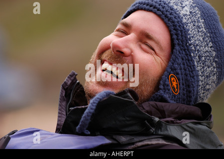 Man wearing a rain jacket and knit cap laughing with his eyes closed Stock Photo