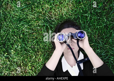 Woman Laying On Grass Looking Into Blue Sky Through Pair Of Field Glasses Stock Photo