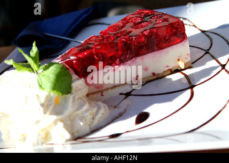 Torta di ricotta e lamponi with smooth cottage cheese purée, fresh raspberries, whipped cream, and mint garnish on a white plate. Stock Photo