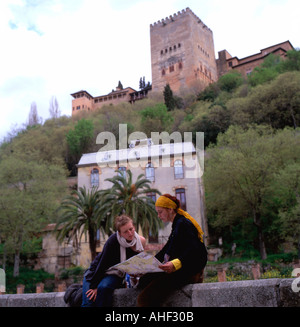 Young women friends sitting on a wall near the River Douro  with a view of the Alhambra Palace map reading in Granada Andalucia Spain EU   KATHY DEWITT Stock Photo