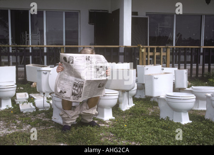 Man Reading Newspaper On one of Many Toilets, Outdoors Stock Photo