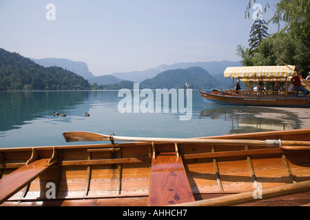 Slovenia Lake Bled in summer with rowing boat and traditional wooden pletnja rowing boat moored on shore Stock Photo