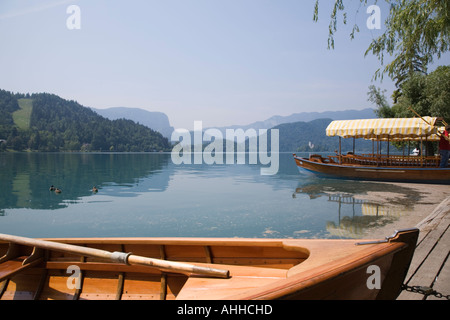 Lake Bled Slovenia in summer with rowing boat and traditional wooden pletnja rowing boat moored on shore Stock Photo