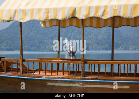 Lake Bled in summer with traditional wooden pletnja rowing boat ferrying tourists from St Mary's Assumption Church on the island Stock Photo