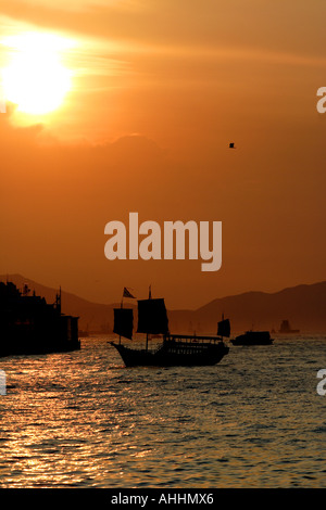Old Chinese Junk in Front of a Golden Red Sunset in Victoria Harbor, Hong Kong Stock Photo
