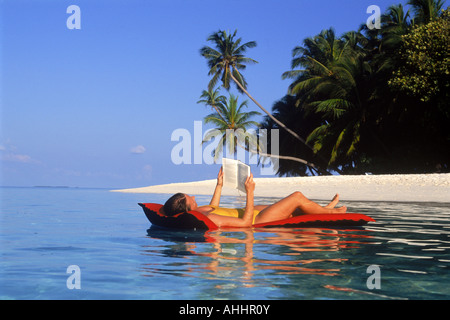 Woman relaxing and reading on air mattress in tropical paradise Stock Photo