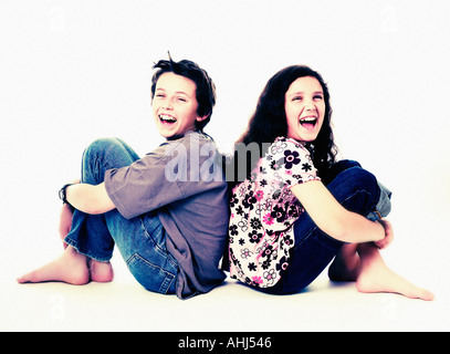 Full length photograph of boy and girl sat back to back laughing Stock Photo