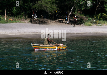 Local man with dreadlocks paddling yellow, green and red boat with beach and trees behind. Anse Chastanet Bay, St. Lucia. Stock Photo