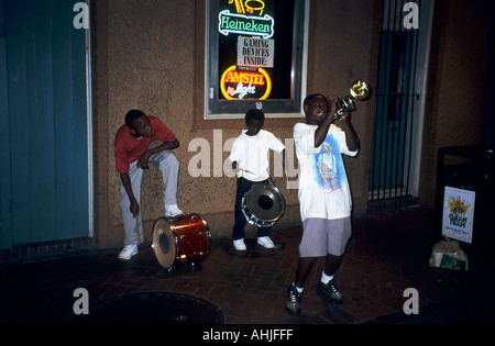 Jazz trio of kids with one trumpet and two drummers play with neon Heineken and Amstel beer signs in window behind. New Orleans, Louisiana, USA. Stock Photo