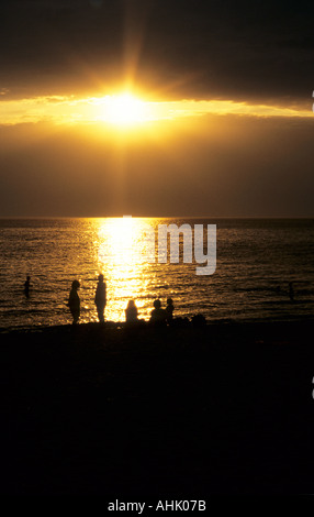 People on St Kilda beach silhouetted against golden light of sunset reflected off water. Melbourne, Victoria, Australia. Stock Photo