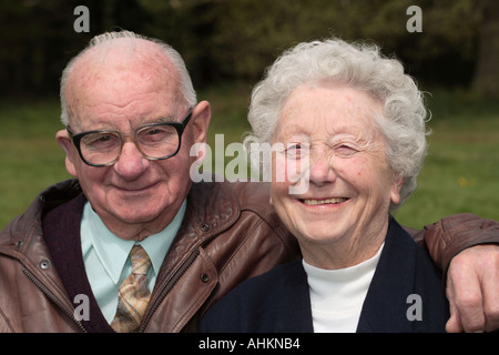 Elderly couple smiling on park bench man with arm around wife Stock Photo
