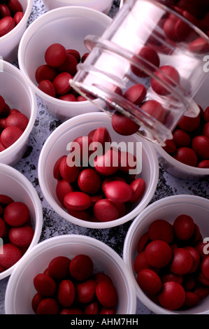 A bottle of red pills being poured in to small cups, vitamins Stock Photo