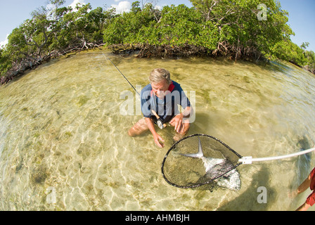 Florida Keys Mature fly fisherman ready to release Permit caught while fly-fishing the Caribbean ocean flats Stock Photo