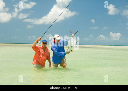 Florida Keys Fly- fisherman and guide land a Permit Fish while fly-fishing the flats of the Caribbean ocean Stock Photo