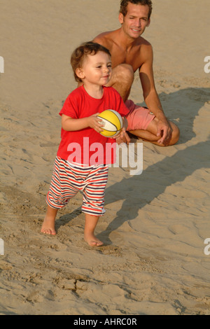A father watches his son play ball on the beach at dusk Stock Photo