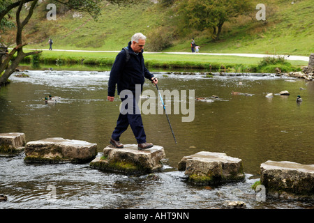male walker crossing the stepping stones over the river dove at dovedale peak district national park derbyshire england uk Stock Photo