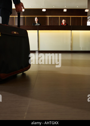 Man wheeling suitcase towards hotel reception desk, low section Stock Photo