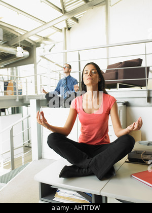 Young adults sitting on office desks in a yoga position Stock Photo