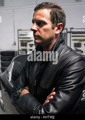 Man leaning on a Porsche in a garage from profile. Stock Photo