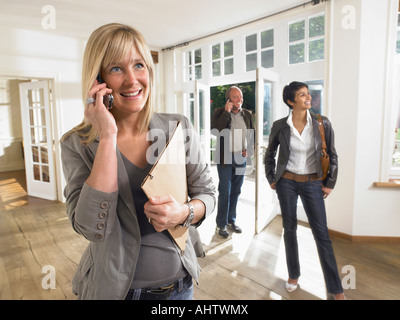 Female real estate agent on phone in show house clients behind. Stock Photo