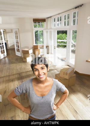 Portrait of a smiling woman moving in empty house. Boxes in background. Stock Photo