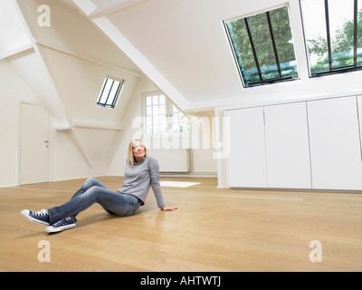 Woman seated on wooden floor of empty white loft. Stock Photo