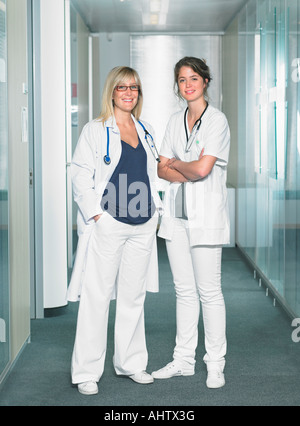 Two female doctors looking at camera in a lobby of a hospital smiling. Stock Photo