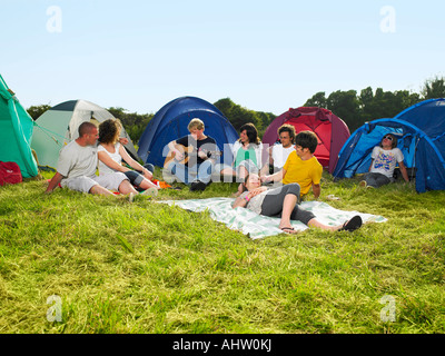 Group sitting outside tents one playing guitar Stock Photo