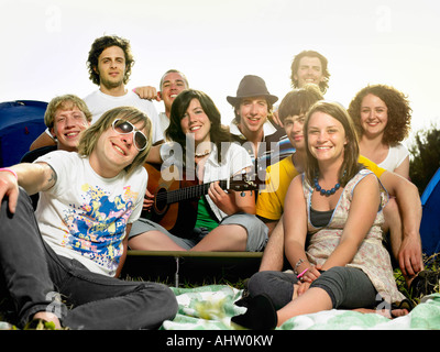 Group smiling at camera sitting outside tents with guitar Stock Photo