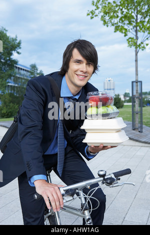 Businessman in park on bike with lots of lunchboxes laughing. Stock Photo
