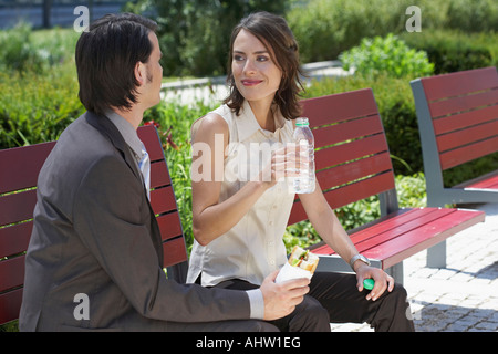 businessman and woman looking at each other with lunch on a bench outdoors Stock Photo