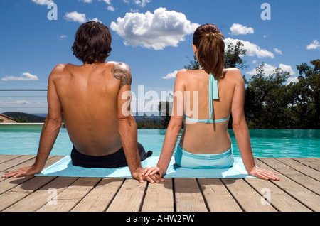 Couple sunbathing by a swimming pool Stock Photo