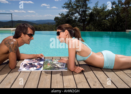 Couple sunbathing by a swimming pool with magazines