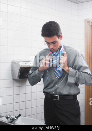 Man reflected in office washroom mirror doing up his tie Stock Photo