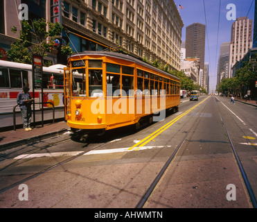 A yellow tramcar pulls up to a stop on a San Francisco street Stock Photo