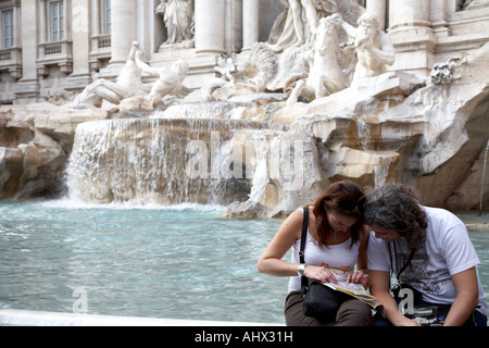 Male and Female tourists consult map sitting on the edge of the Trevi fountain Rome Lazio Italy Stock Photo