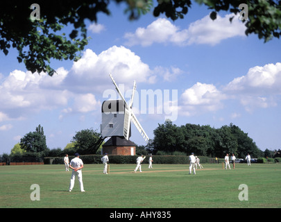 Iconic quintessential England idyllic village green cricket match bowler batsman & fielders Mountnessing Post Mill beyond in Essex countryside UK Stock Photo