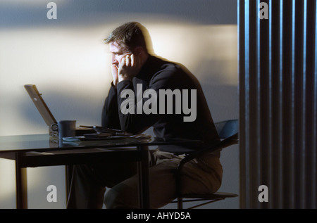 Perplexed man sitting at desk and using laptop computer Stock Photo