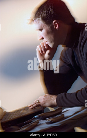Thouhtful Caucasian man sitting at desk using laptop computer Stock Photo