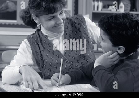 Black and white photo of a Caucasian teacher helping student in elementary school classroom Stock Photo