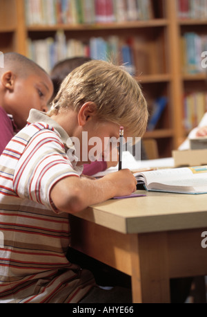Caucasian male student writing book report in Elementary school library Stock Photo