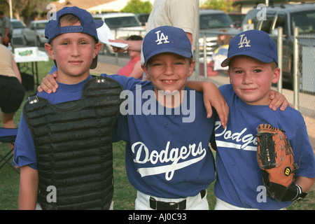 Portrait of three boys in L A Dodgers baseball uniforms posing together off field during a Little League game