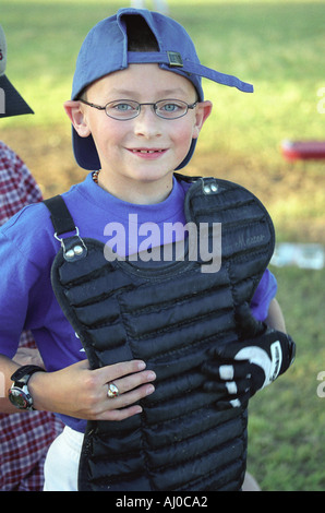 Portrait of a smiling boy in a Little League baseball catcher uniform standing off field between innings