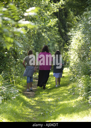 Mother and her two daughters taking a walk along a tree lined country lane in the summer Stock Photo
