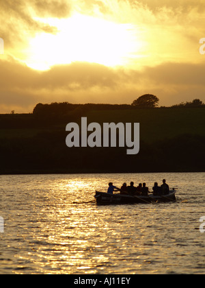 Silhouette of people rowing a boat on Upper Tamar Lakes at sunset, Bude, Cornwall, UK Stock Photo